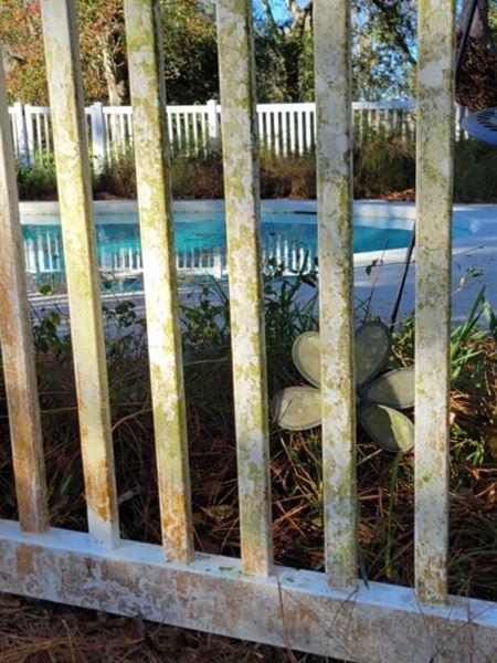 White vinyl pool fence before cleaning, pickets streaked with green algae and orange stains