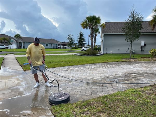 A surface cleaner running across a paver driveway, half of it already clean