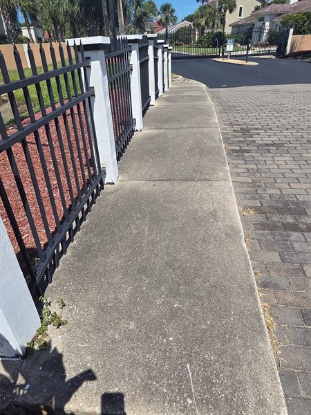 Clean concrete sidewalk along a black iron and white post fence