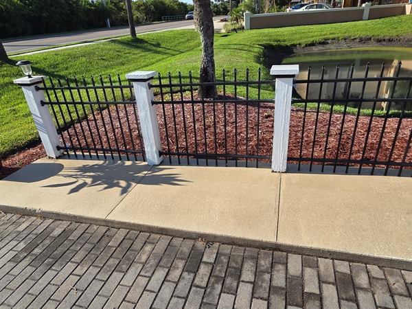 Concrete curb and sidewalk along a black iron fence after cleaning