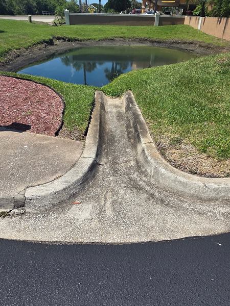 Concrete drainage flume by a retention pond before cleaning, dark with grime