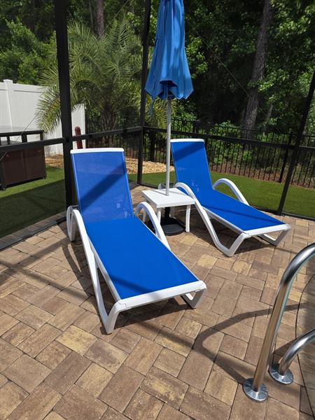 Clean paver pool deck with blue lounge chairs and an umbrella