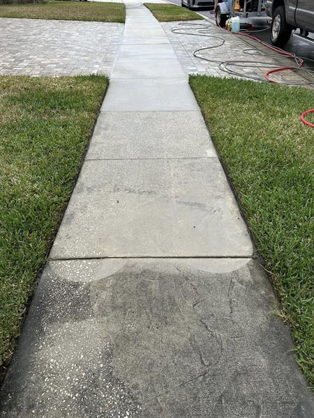 Concrete sidewalk halfway through cleaning, the washed slabs bright and the slabs nearest the camera still dark